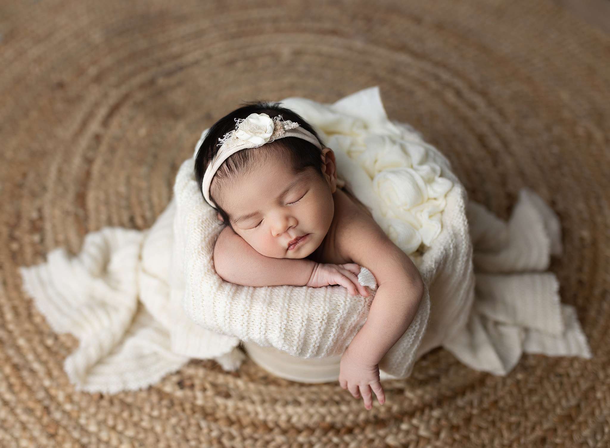 Sleeping newborn baby nestled in a soft basket, photographed with care in a newborn photography session in San Diego