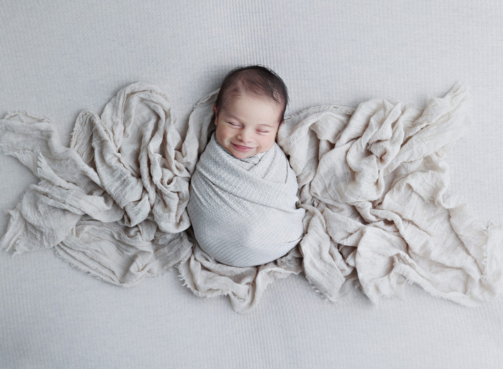 Sleeping smiling newborn baby nestled in a soft blanket, photographed with care in a San Diego newborn photography session.