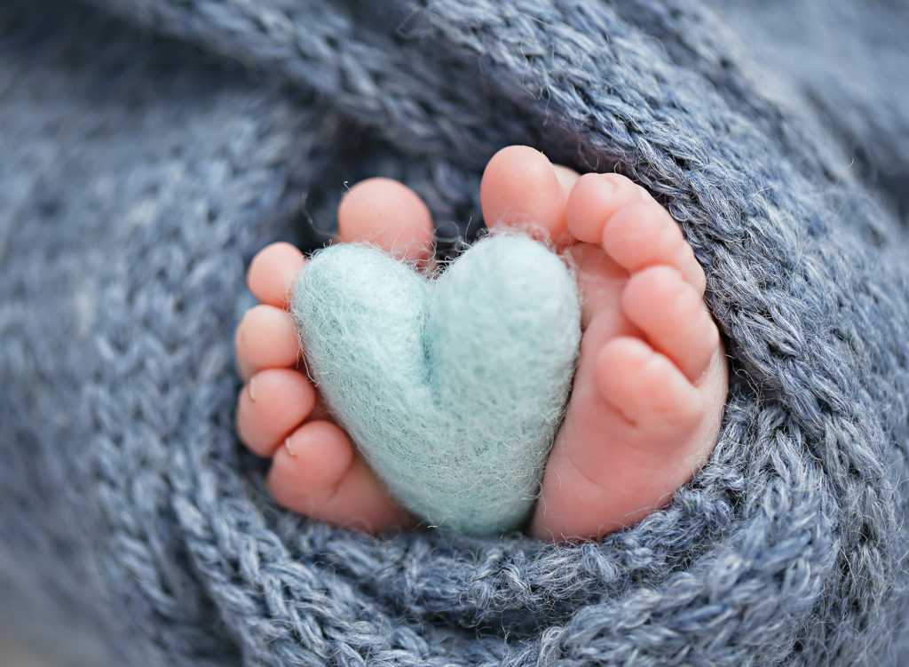 Adorable newborn baby toes holding a felt heart, photographed with care in a professional San Diego newborn photography studio