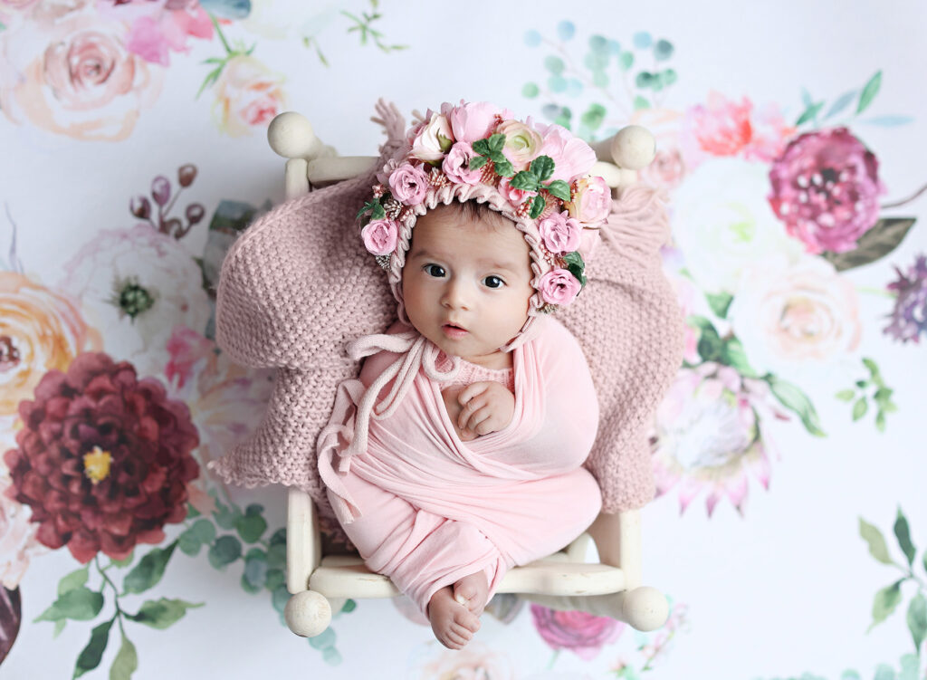 Precious newborn baby girl posed with a flower bonnet, captured by a professional San Diego newborn photographer.