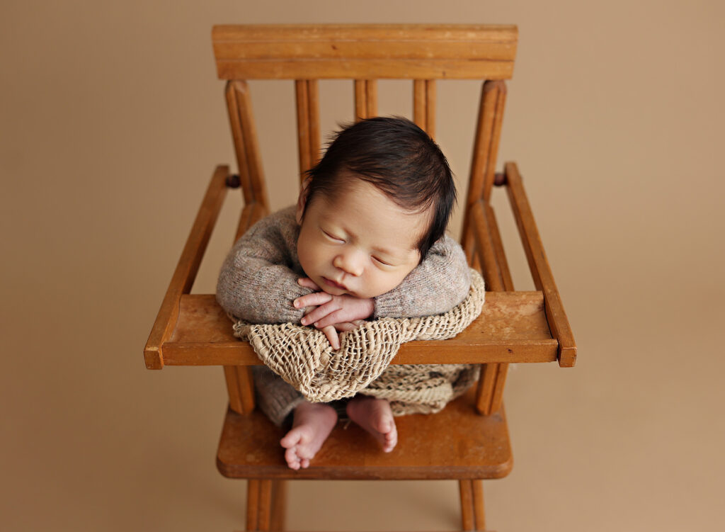 Newborn baby cradled in delicate high chair prop, showcasing the artistry of newborn photography in San Diego